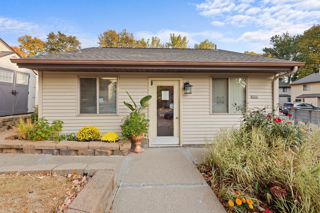 A house with a brown roof and a grey door surrounded by plants and flowers.