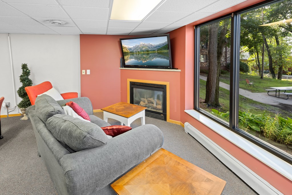 A grey couch with a pillow and a small table in front of a fireplace.