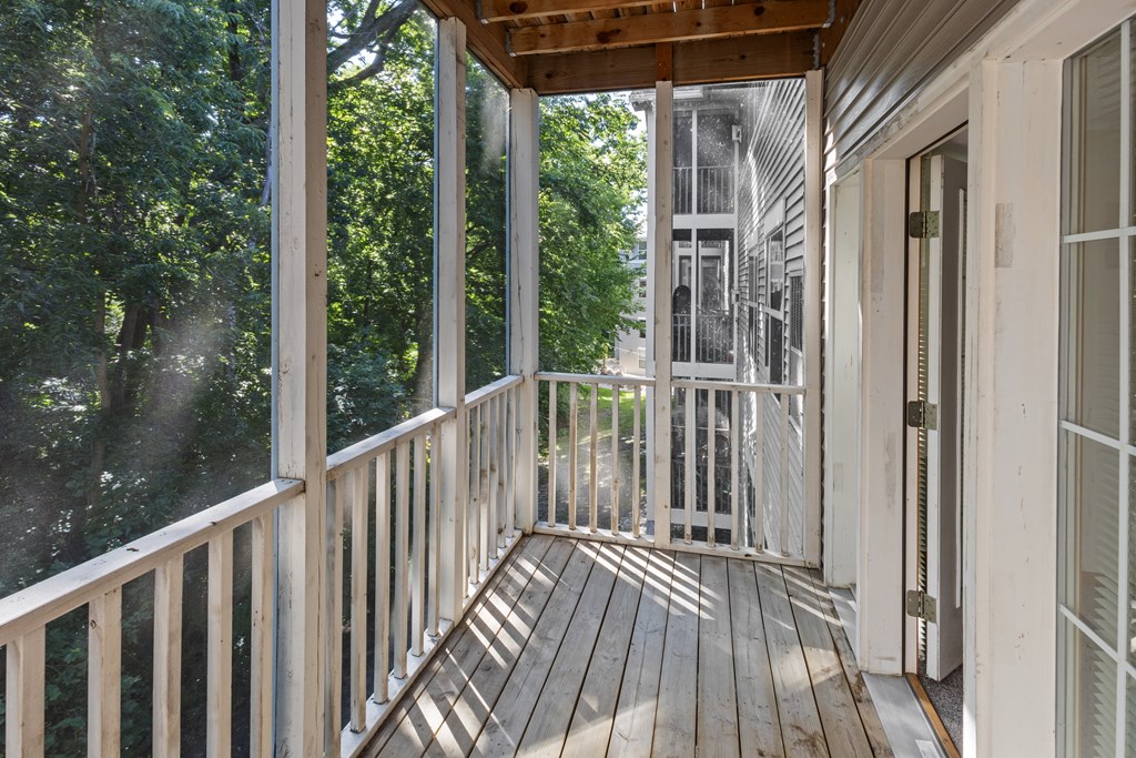 A wooden deck with a railing and a view of trees and a building in the background.