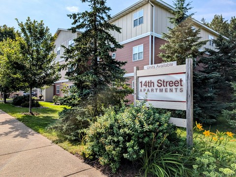 A sign for 14th Street Apartments is in front of a building with a well-kept lawn and trees.