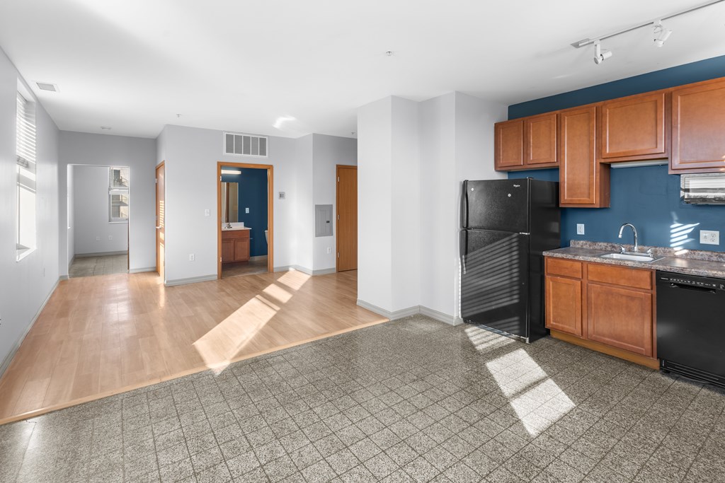 A kitchen area with a black refrigerator and wooden cabinets.