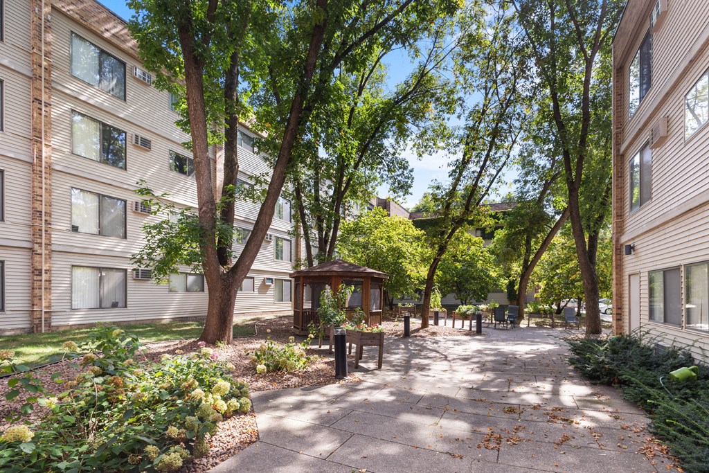 A tree-lined walkway leads to a small pavilion in a courtyard.