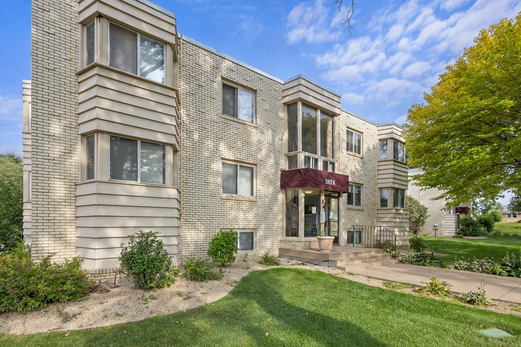 the front of a brick apartment building with green grass and trees