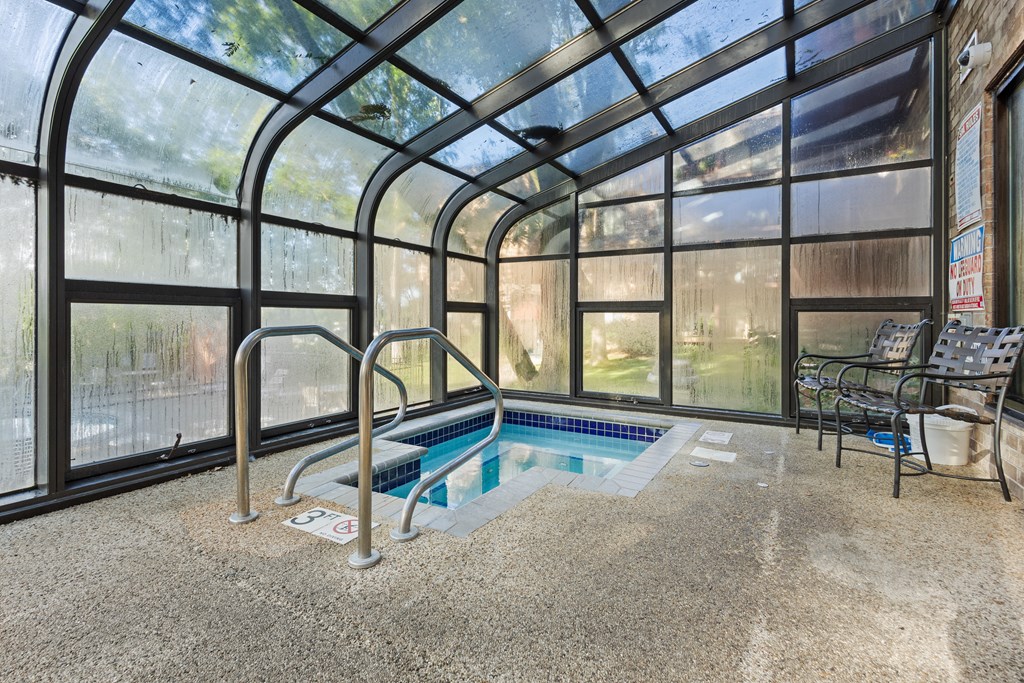 a indoor hot tub in a greenhouse with chairs and a wall of windows