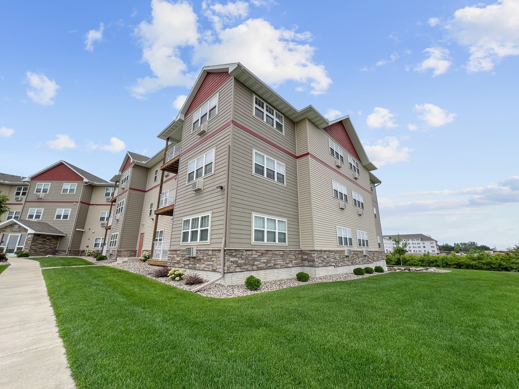 A large apartment building with a red roof and a green lawn in front.