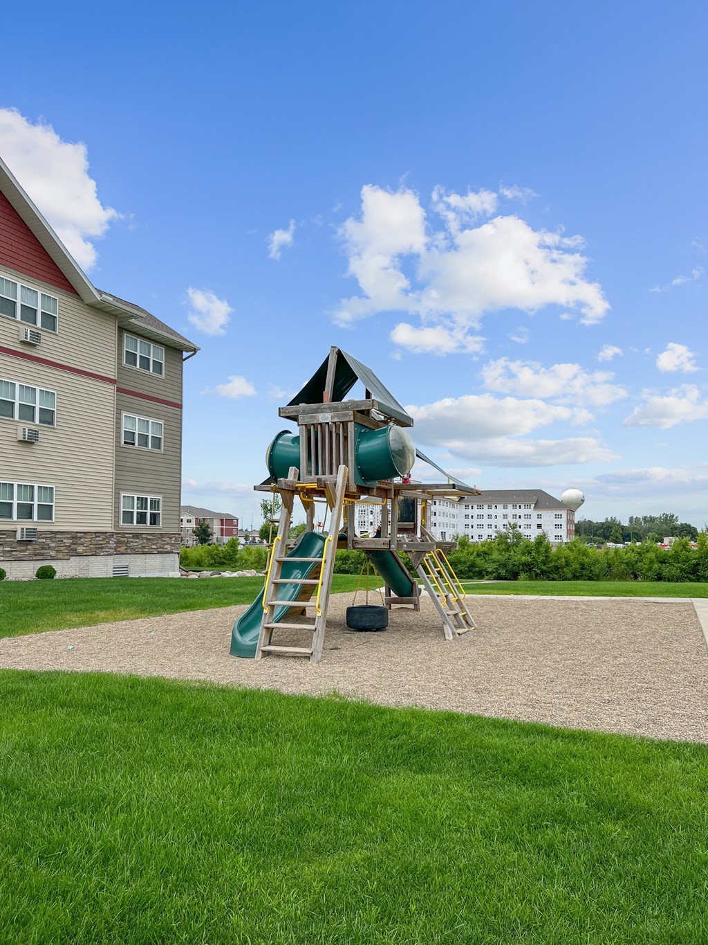 A playground with a green slide and a wooden ladder.