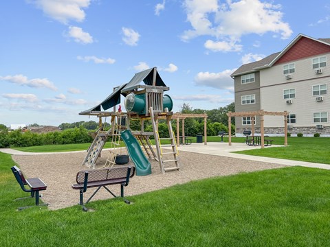 A playground with a green slide and a wooden swing set.