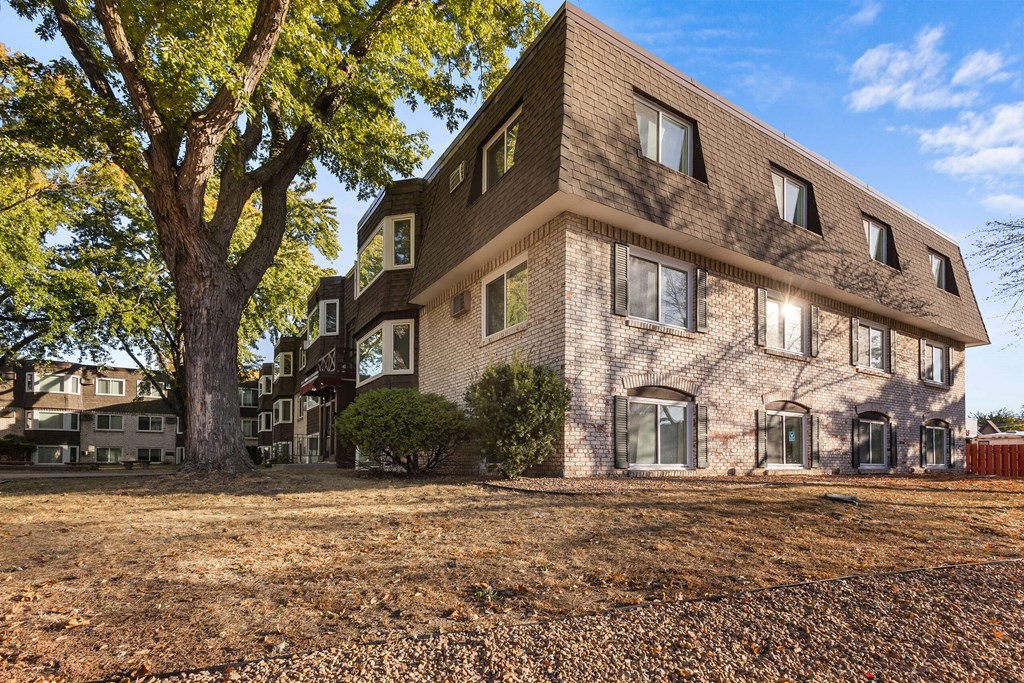 a brick apartment building with a large tree in the yard