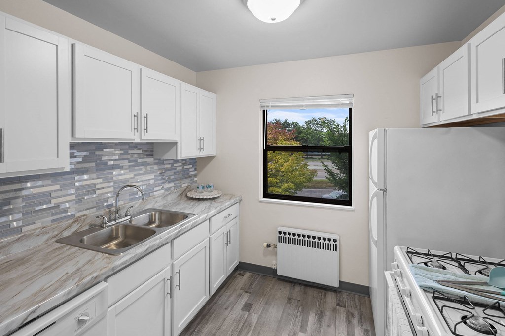 A kitchen with white cabinets and a window overlooking a street.