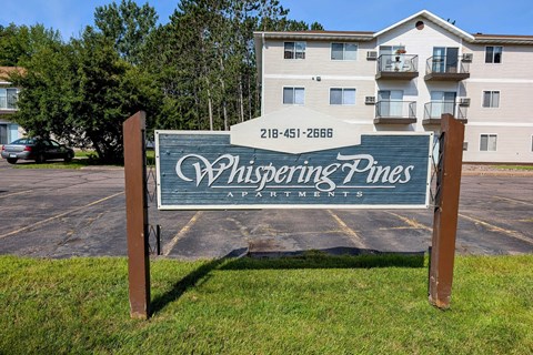 A sign for Whispering Pines Apartments stands in front of a building.