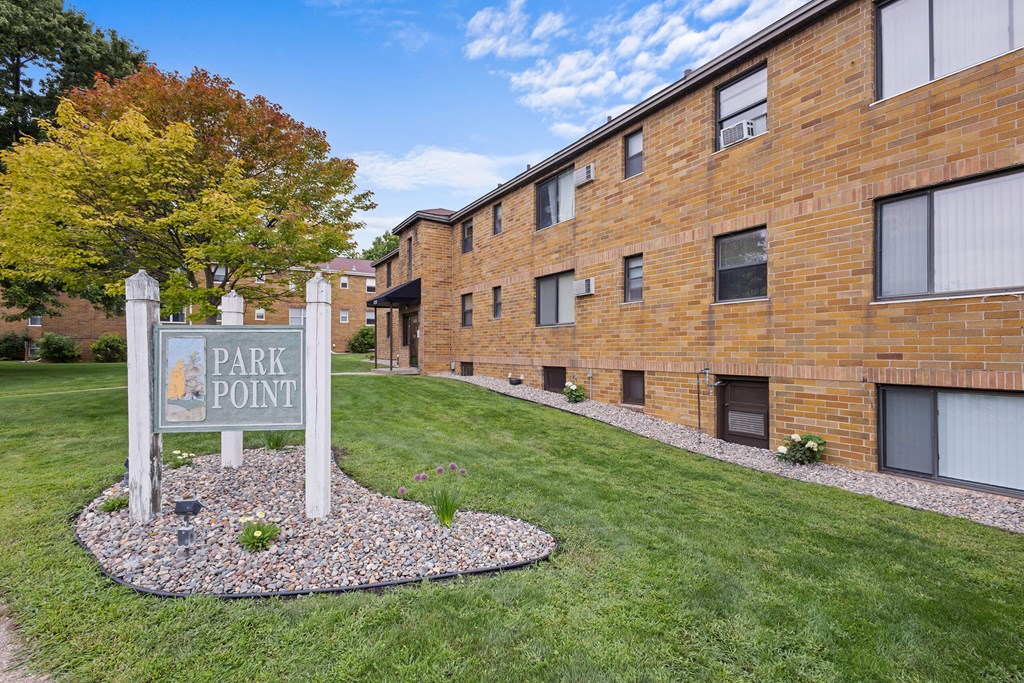 A sign that says Park Point stands in a grassy area in front of a brick building.