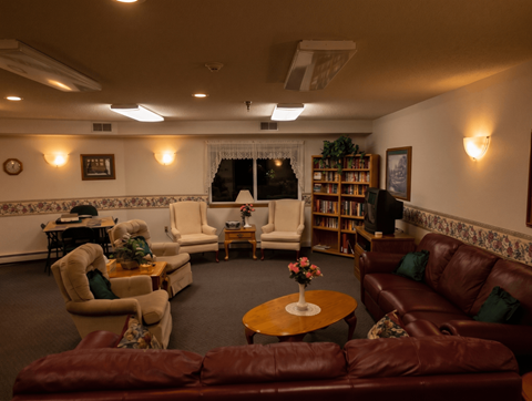 A living room with a brown leather couch and a round table with a vase of flowers on it.