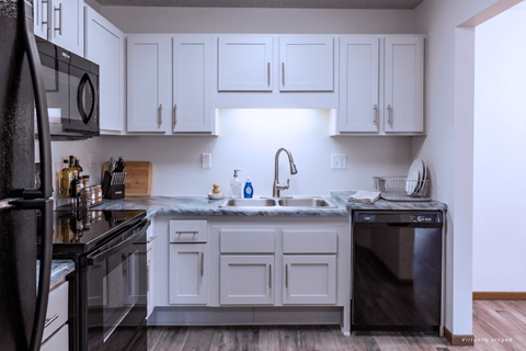 A kitchen with white cabinets and a black refrigerator.