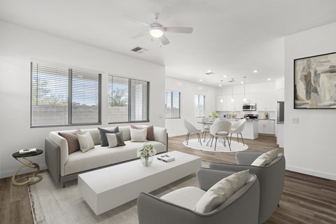 A modern living room with a grey sofa, a white coffee table, and a dining table set up in the background.