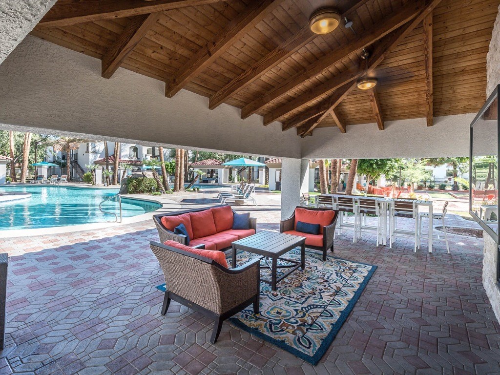 a covered patio with chairs and tables next to a swimming pool