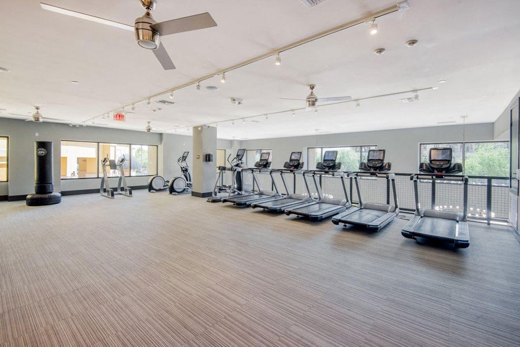 a fitness room with cardio machines and a ceiling fan