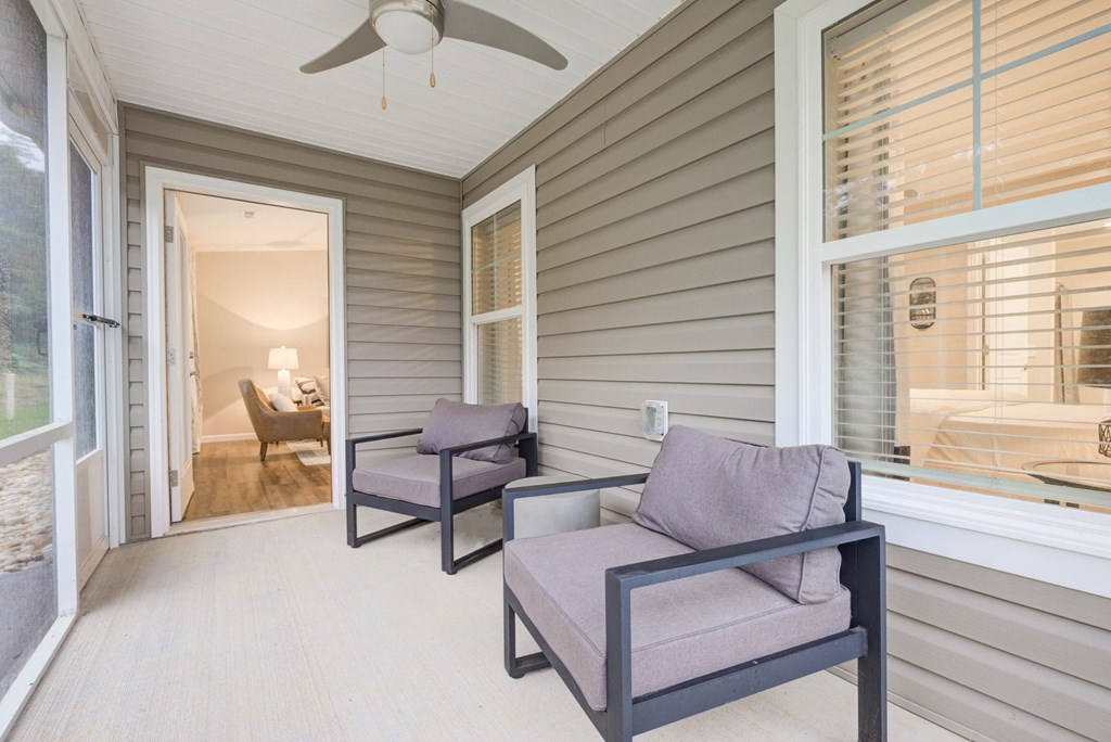 a covered porch with two chairs and a ceiling fan