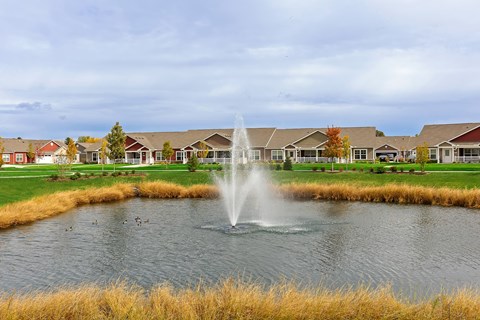 A fountain in the middle of a pond in front of a row of houses.