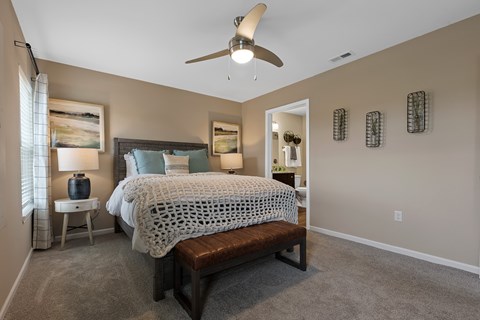 A bedroom with a bed, bench, and a ceiling fan.