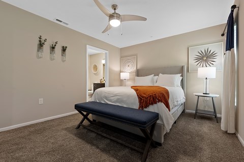 A bedroom with a bed, a bench, and a ceiling fan.