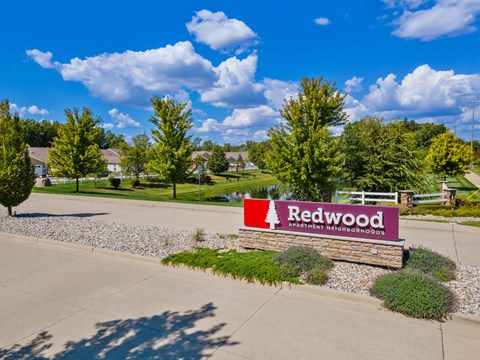 A sign for Redwood Apartments is in front of a grassy area.