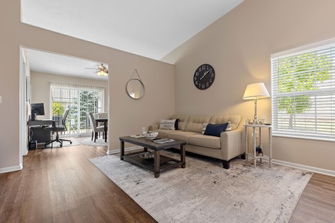 A living room with a couch, a table, a clock, and a window with blinds.