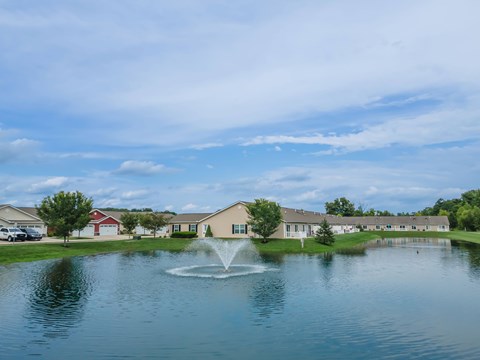 A fountain in the middle of a pond in front of a building.