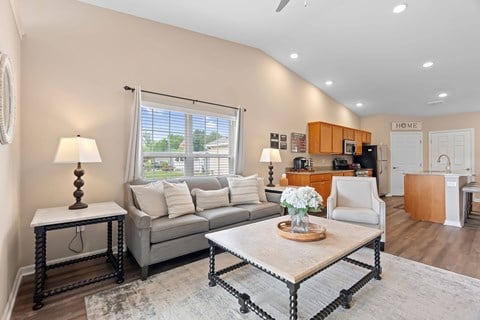 A well-lit living room with a grey sofa, a coffee table, and a side table with a lamp.