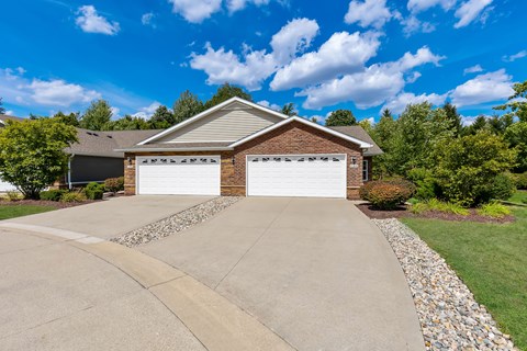 A house with a white garage door is surrounded by a gravel driveway and a grassy lawn.