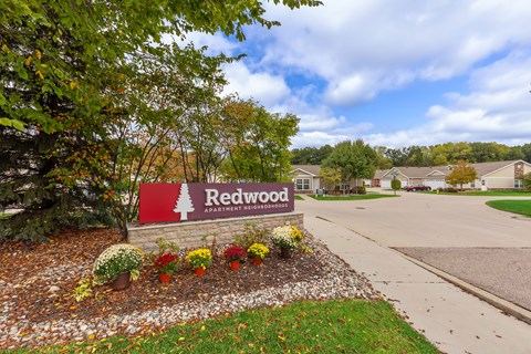 A sign for Redwood Apartments is surrounded by flowers and trees.
