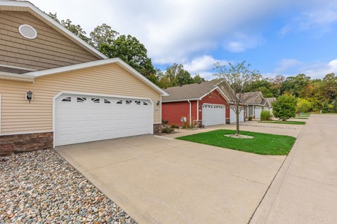 A house with a red garage door is surrounded by a gravel driveway and a grassy area.