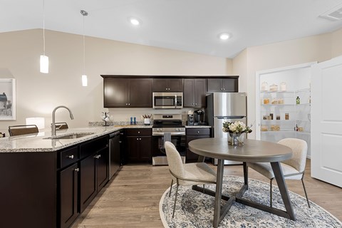 A modern kitchen with dark brown cabinets and a round table with a vase of flowers on it.