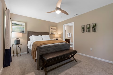 A bedroom with a bed, bench, and a ceiling fan.