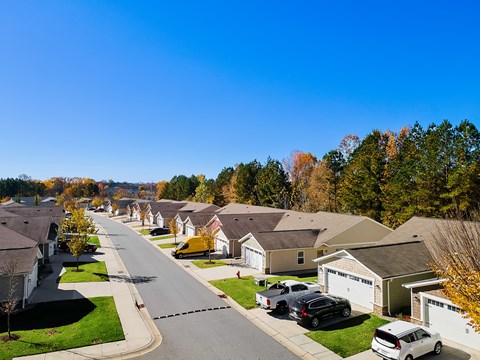 A residential street with houses on both sides and cars parked in front.