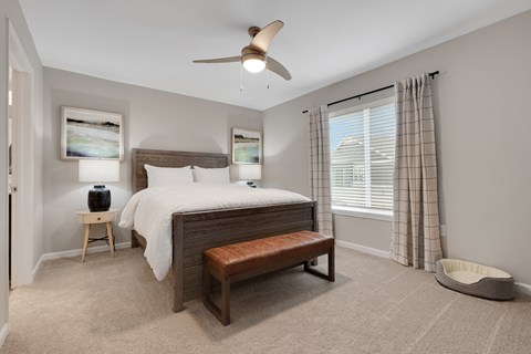A bedroom with a bed, bench, and a ceiling fan.