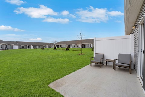 A row of houses with a lawn in front and two chairs on a concrete walkway.