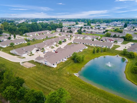 A bird's eye view of a residential area with houses surrounding a pond.