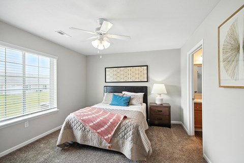 A bedroom with a bed, a ceiling fan, and a window with blinds.