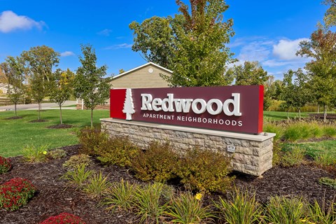 A sign for Redwood Apartment Neighborhoods is displayed in front of a building.