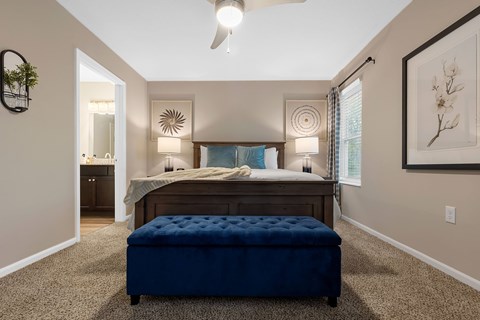 A bedroom with a bed, a bench, and a ceiling fan.