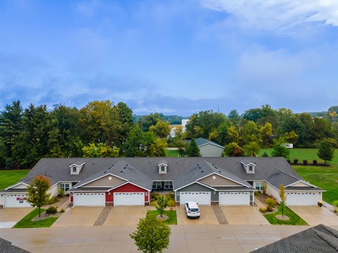A large house with a red garage door is surrounded by a driveway and trees.