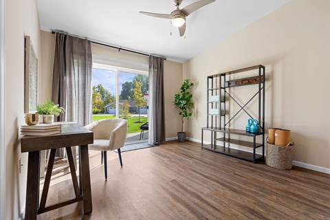 A room with a wooden table and a white chair with a view of the backyard through the window.