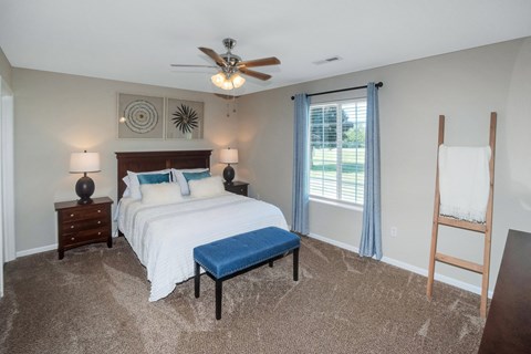 A bedroom with a bed, nightstand, and a window with a view of the outside.