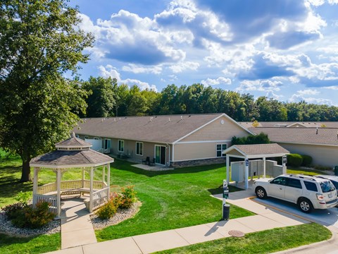 A car is parked in front of a house with a gazebo in the front yard.