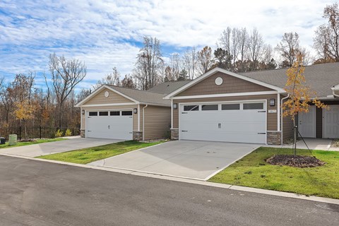 A two-car garage with a brown roof and white doors is surrounded by a concrete driveway and a grassy area.