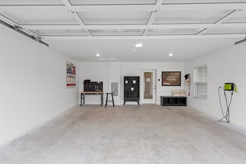 A spacious room with a white ceiling and walls, containing a workbench, a black cabinet, and a green and black object on the floor.