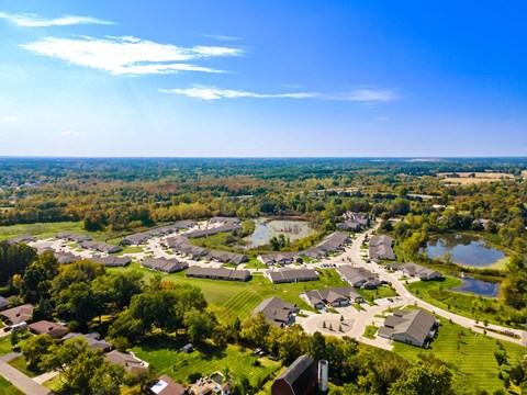 A bird's eye view of a residential area with houses, trees, and a pond.