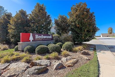 A sign for Redwood Apartment Neighborhoods is displayed in front of some trees.