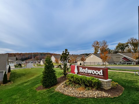 A sign for Redwood Apartment Neighborhoods is in the foreground of a grassy area.