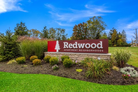A sign for Redwood Apartment Neighborhoods is surrounded by plants and grass.
